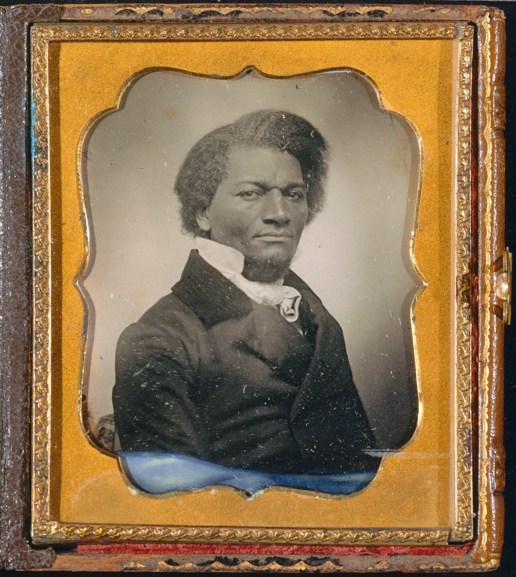 Frederick Douglass posant pour un portrait assis, en tenue du milieu du XIXe siècle.  Le portrait est en noir et blanc et encadré dans un cadre doré.